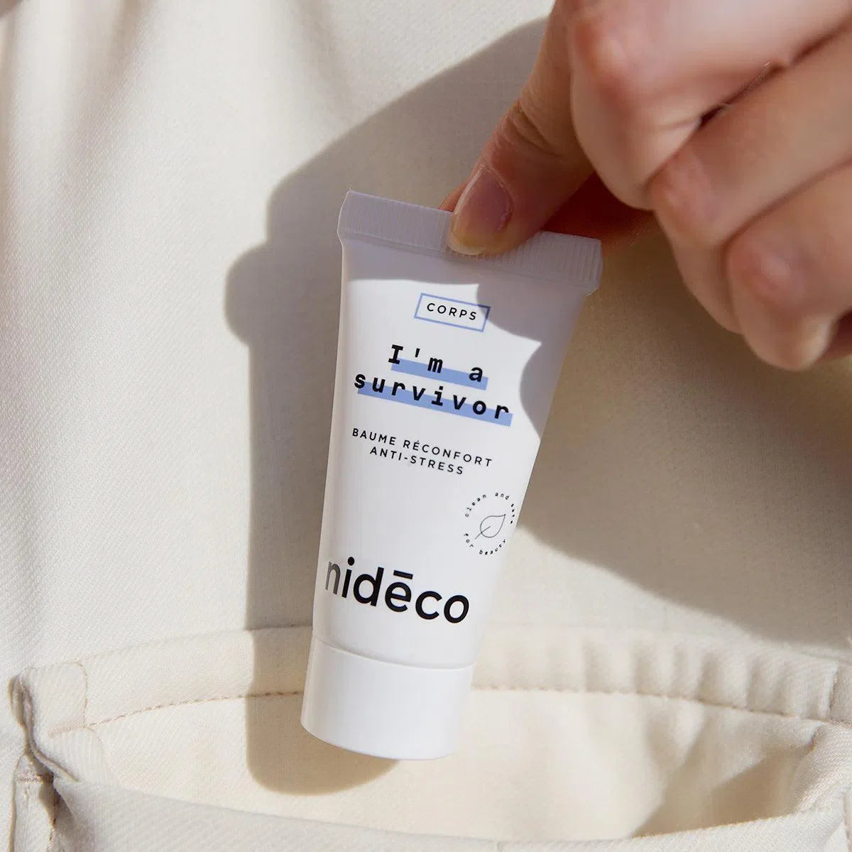 Main qui mets dans une poche le I'm a survivor baume réconfortant anti-stress de Nidéco aux huiles essentielles