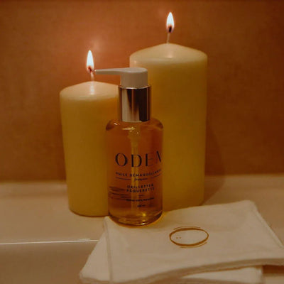 Huile démaquillante sans coton aux paquerettes et aux oeillettes de Oden  avec des bougies sur un lavabo