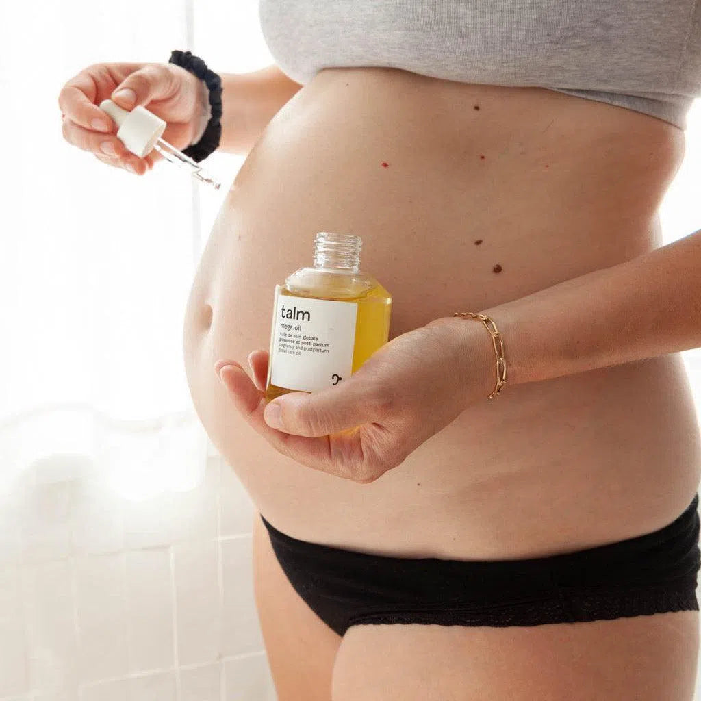 Femme enceinte qui applique sur son ventre l'huile de soin corps et visage nourrissante pour nourrir et prévenir les vergetures de Talm