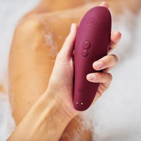 Main qui tient un sextoy clitoridien à air pulsée Classic 2 violet de Womanizer dans un bain